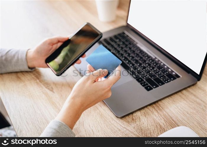 Asian woman holding credit card paying for shopping on mobile phone with computer laptop on wooden table