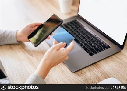 Asian woman holding credit card paying for shopping on mobile phone with computer laptop on wooden table