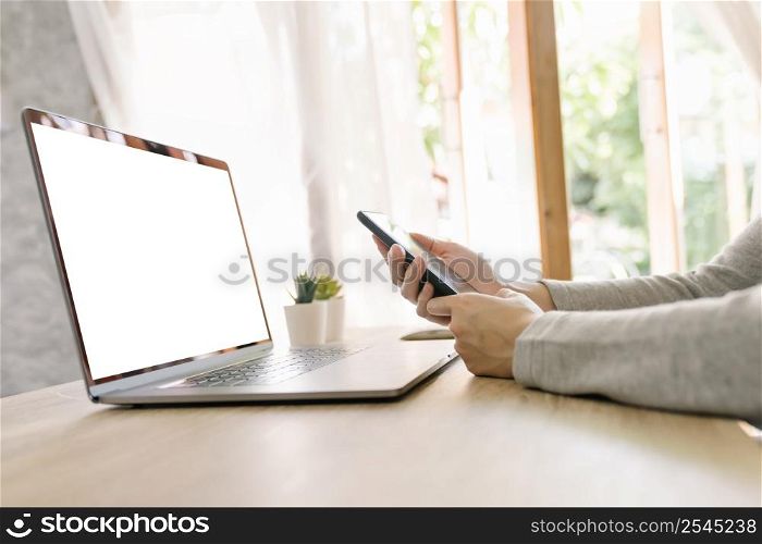 Asian woman holding phone and using computer laptop on wooden table
