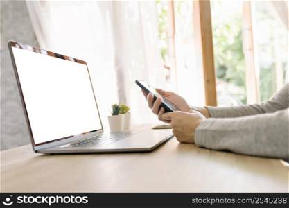 Asian woman holding phone and using computer laptop on wooden table