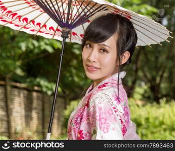 Asian woman in a kimono in a Japanese style garden holding an umbrella