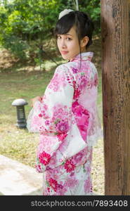 Asian woman in a kimono in a Japanese style garden leaning against pillar