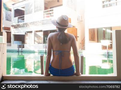 Asian woman in blue colour bikini sitting near swimming pool. Travel vacation or beauty concept