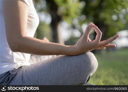Asian woman in lotus pose sitting on green grass and a blurred background in the park, Concept of relaxation and meditation