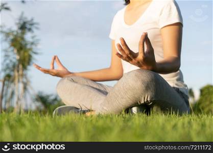 Asian woman in lotus pose sitting on green grass and blurred background in the park, Concept of relaxation and meditation
