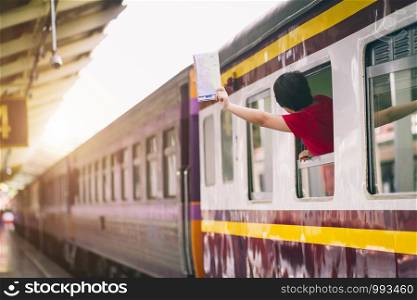 Asian woman in red dress holding a map and hand up say hello on the train. travel railway station travel.