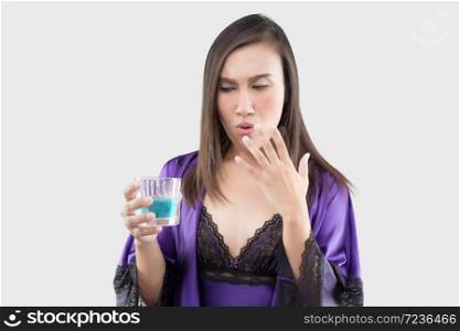 Asian woman in sexy silk nightgown and purple robe feel burn in her mouth because using mouthwash against a gray background, Wash the mouth, Female rinsing and gargling while using mouthwash from a glass