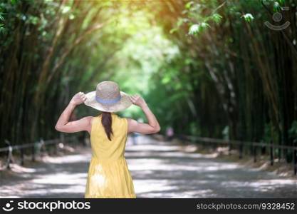 Asian Woman in yellow dress and hat Traveling at green Bamboo Tunnel, Happy traveler walking Chulabhorn wanaram temple. landmark and popular for tourists attractions in Nakhon Nayok, Thailand