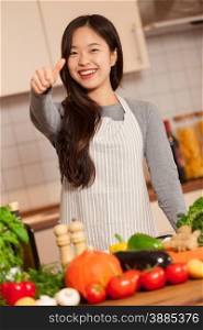 Asian woman is making positive thumb gesture in a kitchen