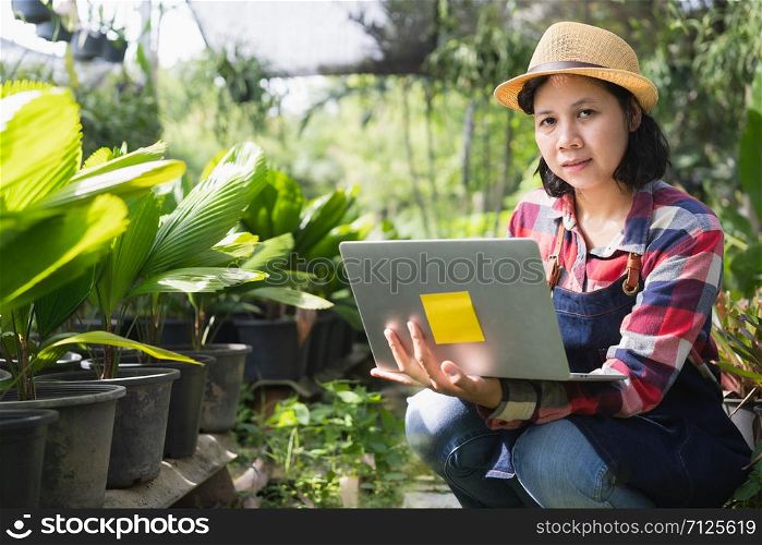 Asian woman is using a laptop to check the vegetation in the Ornamental plant shop, Small business concept