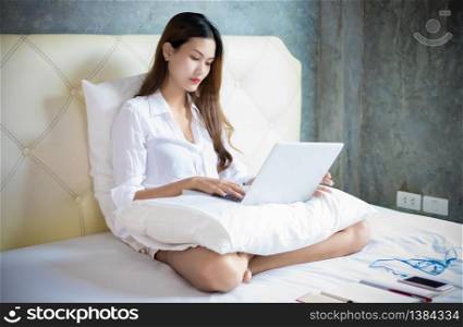 Asian woman is using a notebook computer for work at home and she is sitting on her bed and she is quarantine during the coronavirus epidemic.