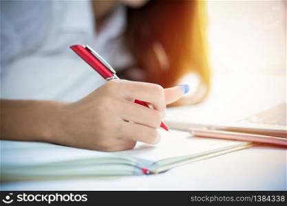 Asian woman is using a pen to write notes in her notebook and she uses a notebook to work on her bed at home.