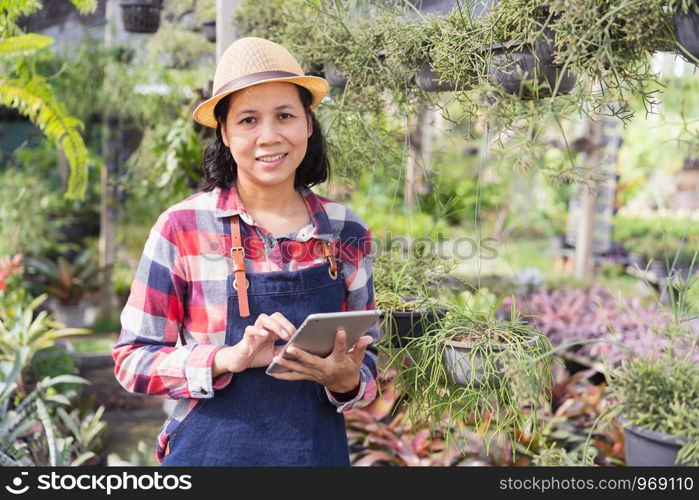 Asian woman is using a tablet to check the vegetation in the Ornamental plant shop, Small business concept