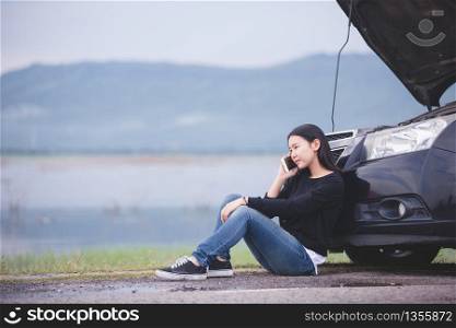 Asian woman is using a telephone to call the car mechanic. For fixing damaged cars on the road