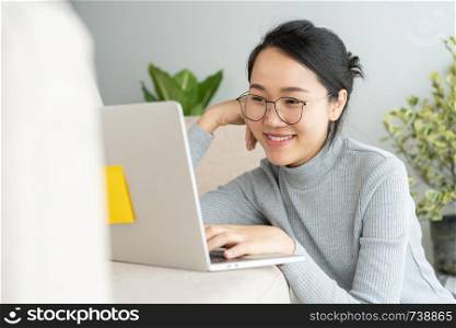 Asian woman is working on a laptop in home . On her face are smile when she work at sofa.