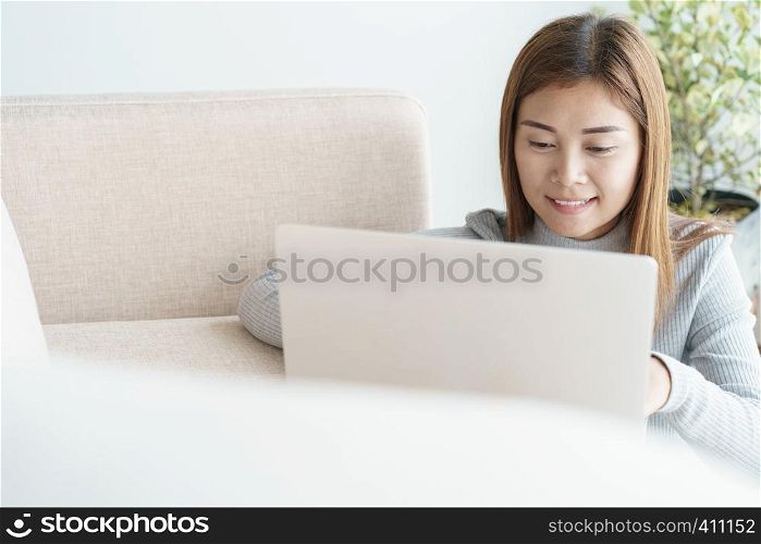 Asian woman is working on a laptop in the living room. She sit on the floor and sofa is office desk.