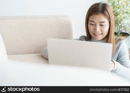 Asian woman is working on a laptop in the living room. She sit on the floor and sofa is office desk.