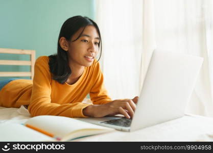 Asian woman learning online with a tutor via the internet with a laptop, Asia student girl video conference on a computer while lying on a bed in the morning, Concept online learning at home