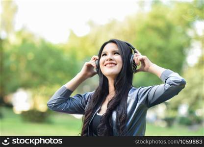 Asian woman listen to music with mobile phone outdoor / Happy young girl smiling relax exercise and listening to music with earphone in the garden park