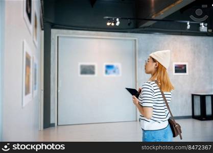 Asian woman note information to tablet at art gallery collection in front framed paintings looking pictures on wall, Young person at photo frame write digital book at show exhibit artwork gallery