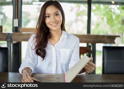 Asian woman open menu for ordering in coffee cafe and restaurant and smiling for happy time