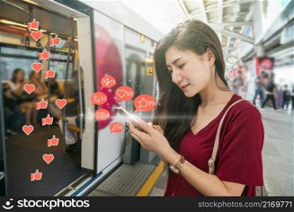 Asian woman passenger using mobile phone to check social network application with number of Like, Love, comment, people and fovorite icon in the Skytrain rails or subway in city, Social media concept,