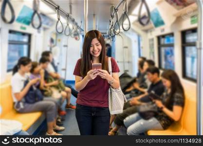 Asian woman passenger with casual suit using the smart mobile phone in the Skytrain rails or subway for travel in the big city, lifestyle and transportation concept
