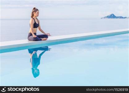 Asian woman practice yoga lotus pose on the pool above the beach in the morning,Feeling so comfortable and relax in holiday