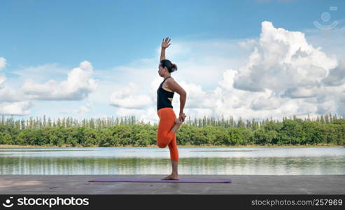 Asian woman practicing yoga pose , exercise outdoors with view of beautiful lake - relax in nature. Asian woman practicing yoga pose