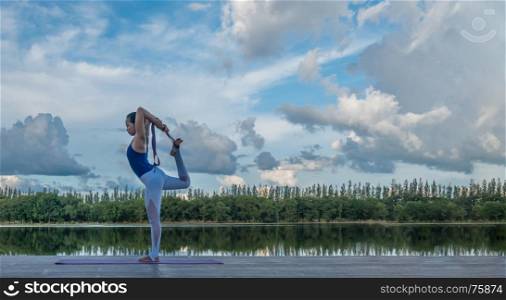 Asian woman practicing yoga pose , exercise outdoors with view of beautiful lake - relax in nature. Asian woman practicing yoga pose