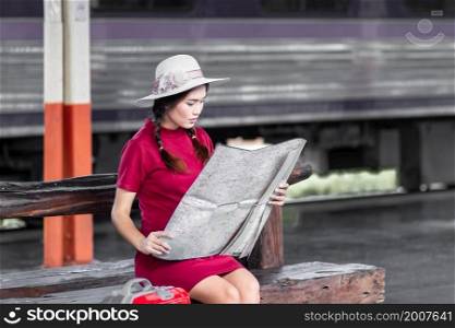 Asian woman pregnant in red dress carrying red luggage and look at the map at railway station travel,traveler with backpack in summer Holiday concept Thailand