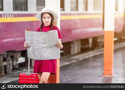 Asian woman pregnant in red dress carrying red luggage and look at the map at railway station travel,traveler with backpack in summer Holiday concept Thailand