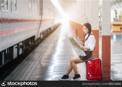 Asian woman pregnant in red dress carrying red luggage and look at the map at railway station travel.