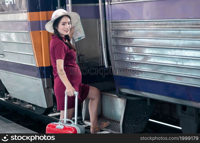 Asian woman pregnant in red dress holding a map with red suitcase at railway station travel,traveler with backpack in summer Holiday concept Thailand