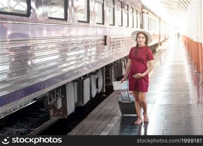 Asian woman pregnant in red dress holding a map with red suitcase at railway station travel,traveler with backpack in summer Holiday concept Thailand