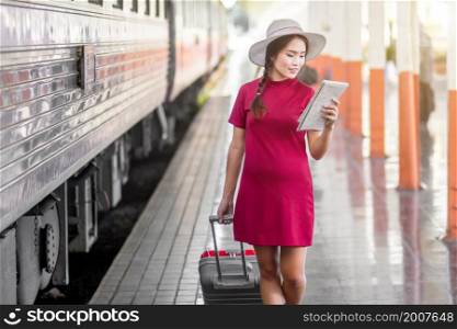 Asian woman pregnant in red dress holding a map with red suitcase at railway station travel,traveler with backpack in summer Holiday concept Thailand