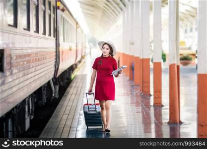 Asian woman pregnant of red dress travel with red suitcase in railway station travel.