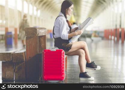 Asian woman pregnant sit on the bench look at the map with red suitcase at railway station travel,Holiday travel concept.
