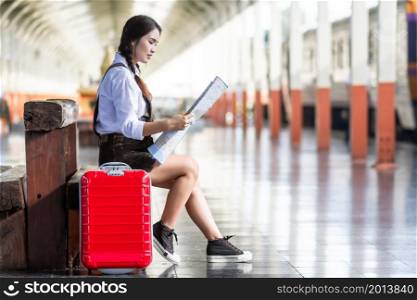 Asian woman pregnant tourist waiting sit on the bench look at the map with red suitcase at railway station travel,traveler with backpack in summer Holiday concept Thailand