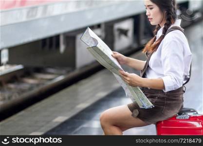 Asian woman pregnant tourist waiting sit on the bench look at the map with red suitcase at railway station travel,traveler with backpack in summer Holiday concept Thailand