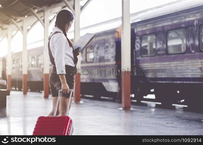 Asian woman pregnant travel look at the map with red suitcase at railway station travel,Holiday travel concept.