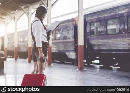 Asian woman pregnant travel look at the map with red suitcase at railway station travel,Holiday travel concept.