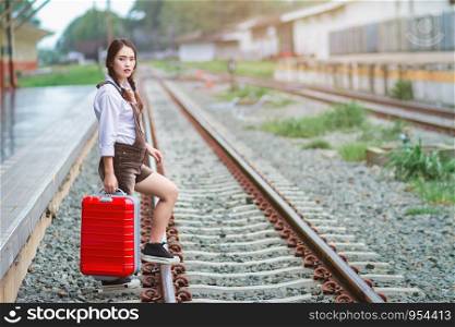 Asian woman pregnant traveler waiting at in a train station carrying her trolley red bag,Belly girl.