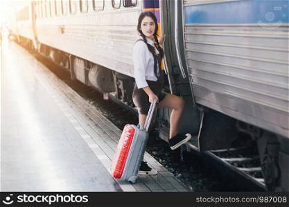 Asian woman pregnant travelers are taking a train with carrying her trolley red bag at the railway station travel.