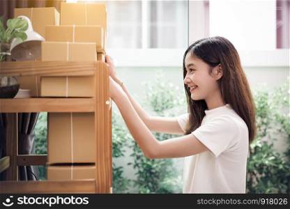 Asian woman put sticky memo paper note on parcel mail box and ready to send to customer. Business owner and Online shopping concept. Post office delivery and home service order entrepreneur theme.
