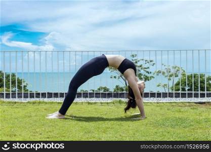 Asian woman relaxing in yoga bridge Pose stretching exercises muscle for warm up on the beach in with seaside,Feeling so comfortable and relax in holiday