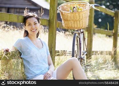 Asian Woman Resting By Fence With Old Fashioned Cycle