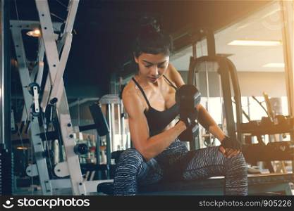 Asian woman's arm holding dumbbell and pull up with strong abs at fitness gym.