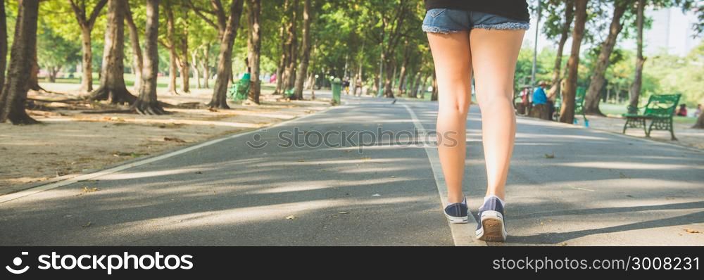 Asian woman&rsquo;s legs while jogging in the park covered with plenty of trees and warm sunlight. Young woman legs close up when running in the park. Outdoor activity in the park concept. Panoramic banner.