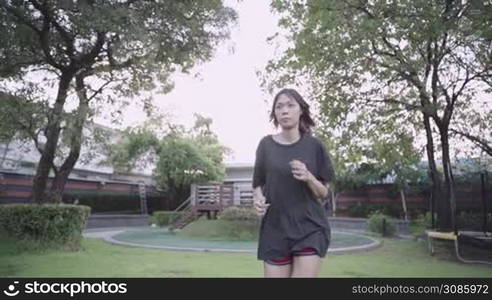 asian woman running on the grass field under trees inside public park, spending time for herself, stay healthy during lockdown pandemic, human metabolic system, diet calories intake, sport motivation